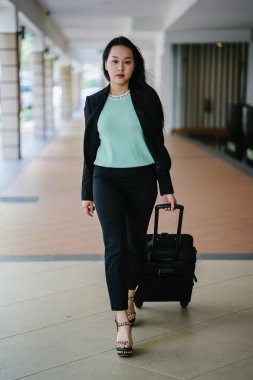 Genç bir Asyalı kadın bavulunu çekiyor. O çekici, zarif ve şık giyinmiş