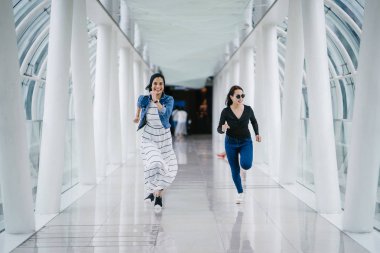 İki farklı arkadaş, iyi aydınlatılmış beyaz fütüristik bir üstgeçit köprüsünden kameraya doğru koşuyorlar. Biri Müslüman bir Orta Doğulu kadın, diğeri de Çinli..