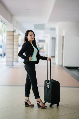Genç bir Asyalı kadın bavulunu çekiyor. O çekici, zarif ve şık giyinmiş