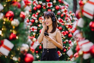 Gün boyunca birkaç süslü Noel ağaçları arasında duran zarif ve çekici bir orta yaşlı kadın portresi