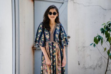 uzun boylu, zarif ve güzel Hint Asyalı kadın yaz elbise ve güneş gözlüğü gülümsüyor o pozlar gün boyunca bir arka sokakta bir sokakta olarak içinde