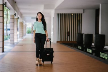 Genç bir Asyalı kadın bavulunu çekiyor. O çekici, zarif ve şık giyinmiş