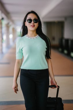 Genç bir Asyalı kadın bavulunu çekiyor. O çekici, zarif ve şık giyinmiş