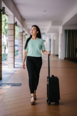 Genç bir Asyalı kadın bavulunu çekiyor. O çekici, zarif ve şık giyinmiş
