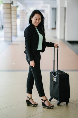 Genç bir Asyalı kadın bavulunu çekiyor. O çekici, zarif ve şık giyinmiş