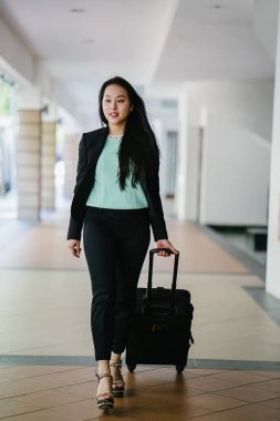 Genç bir Asyalı kadın bavulunu çekiyor. O çekici, zarif ve şık giyinmiş