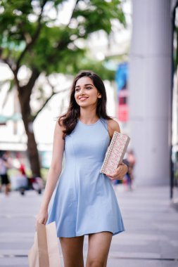 genç, son moda ve mutlu genç Hintli Asyalı kadın alışveriş bölgesine bir sokakta yürürken bir mavi elbiseli 