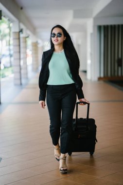 Genç bir Asyalı kadın bavulunu çekiyor. O çekici, zarif ve şık giyinmiş