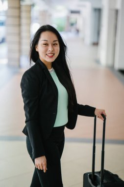 Genç bir Asyalı kadın bavulunu çekiyor. O çekici, zarif ve şık giyinmiş