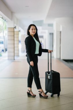 Genç bir Asyalı kadın bavulunu çekiyor. O çekici, zarif ve şık giyinmiş