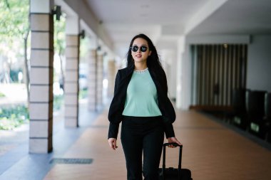 Genç bir Asyalı kadın bavulunu çekiyor. O çekici, zarif ve şık giyinmiş