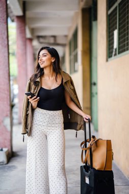 Genç ve çekici Asyalı Hint kadın arabayla aracılığıyla onun yolculuğu app onun akıllı yağıyor kitaplar. O bir geçit kendi bavullarla duruyor ve şık iş giysisi ve tonları giymiş