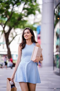 genç, son moda ve mutlu genç Hintli Asyalı kadın alışveriş bölgesine bir sokakta yürürken bir mavi elbiseli 