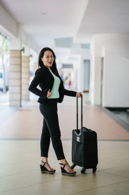 Genç bir Asyalı kadın bavulunu çekiyor. O çekici, zarif ve şık giyinmiş