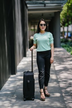 Genç bir Asyalı kadın bavulunu çekiyor. O çekici, zarif ve şık giyinmiş