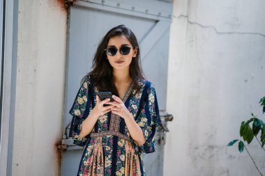 Bir elbise ve onun smartphone ile güneş gözlüğü takan bir genç, çekici ve güzel Hint Asyalı kadın portresi