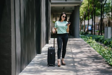 Genç bir Asyalı kadın bavulunu çekiyor. O çekici, zarif ve şık giyinmiş