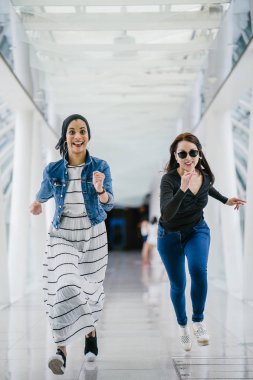 İki farklı arkadaş, iyi aydınlatılmış beyaz fütüristik bir üstgeçit köprüsünden kameraya doğru koşuyorlar. Biri Müslüman bir Orta Doğulu kadın, diğeri de Çinli..