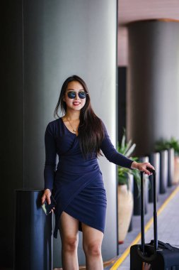 Genç bir Asyalı kadın bavulunu çekiyor. O çekici, zarif ve şık giyinmiş