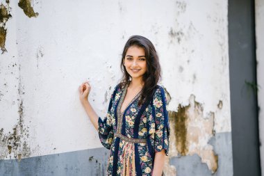 bir sokakta yıpranmış bir duvara portre genç bir uzun boylu, zarif ve güzel Hint Asyalı kadın akan içinde elbise 