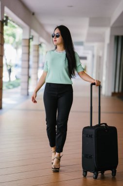 Genç bir Asyalı kadın bavulunu çekiyor. O çekici, zarif ve şık giyinmiş