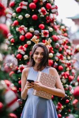 Genç, güzel ve mutlu bir Hint Asyalı kadın şenlikli Noel portresi bir hediye bir Noel ağacı önünde tutan gülümseyerek.