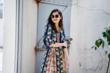 uzun boylu, zarif ve güzel Hint Asyalı kadın yaz elbise ve güneş gözlüğü gülümsüyor o pozlar gün boyunca bir arka sokakta bir sokakta olarak içinde