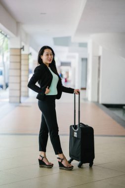 Genç bir Asyalı kadın bavulunu çekiyor. O çekici, zarif ve şık giyinmiş
