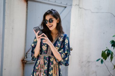 Bir elbise ve onun smartphone ile güneş gözlüğü takan bir genç, çekici ve güzel Hint Asyalı kadın portresi