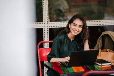 genç üniversite öğrencisi (Hint Asyalı kadın) eğitim ve gün boyunca dizüstü bilgisayar bir masa başında çalışma