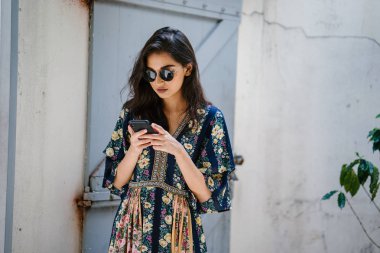 Bir elbise ve onun smartphone ile güneş gözlüğü takan bir genç, çekici ve güzel Hint Asyalı kadın portresi