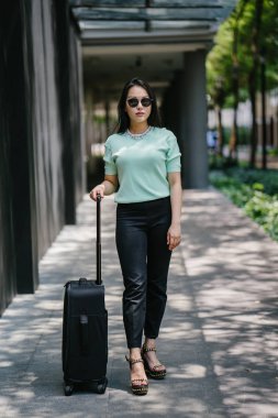 Genç bir Asyalı kadın bavulunu çekiyor. O çekici, zarif ve şık giyinmiş
