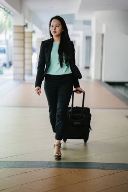 Genç bir Asyalı kadın bavulunu çekiyor. O çekici, zarif ve şık giyinmiş