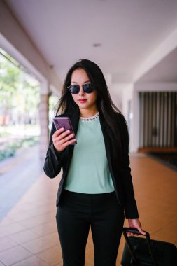 O bir yolculuk dolu uygulama üzerinden rezervasyonu onu binmek için caddenin kenarında bekleyen zarif ve güzel bir genç Asyalı kadının portresi. Tekerlekli bir bavula tutunuyor.. 