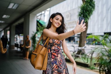 Genç, güzel ve zarif Punjabi Hint Asyalı kadın kendini bir selfie onun smartphone ile yoğun bir cadde üzerinde gün boyunca alır