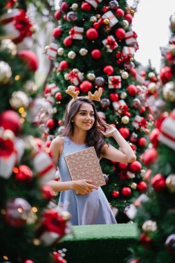 Genç, güzel ve mutlu bir Hint Asyalı kadın şenlikli Noel portresi bir hediye bir Noel ağacı önünde tutan gülümseyerek.