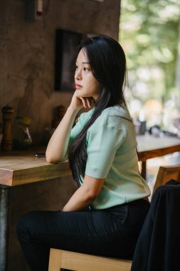 Genç ve çekici Çinli Asyalı bir kadının portresi uzanarak ve bir hafta sonu gün boyunca bir kafede rahatlatıcı. Nane yeşili bir kazak giyiyor.