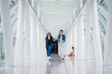 İki farklı arkadaş, iyi aydınlatılmış beyaz fütüristik bir üstgeçit köprüsünden kameraya doğru koşuyorlar. Biri Müslüman bir Orta Doğulu kadın, diğeri de Çinli..