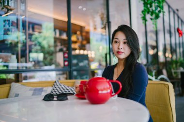 Bir açık havada açık havada oturan ve kırmızı bir çay seti çay sıcak bir fincan zevk genç, çekici, zarif ve güzel Asyalı kadın Portresi. 