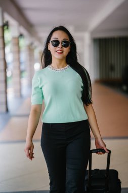 Genç bir Asyalı kadın bavulunu çekiyor. O çekici, zarif ve şık giyinmiş