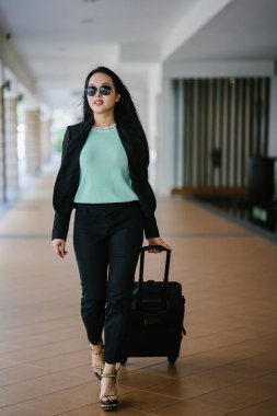 Genç bir Asyalı kadın bavulunu çekiyor. O çekici, zarif ve şık giyinmiş