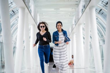 İki farklı arkadaş, iyi aydınlatılmış beyaz fütüristik bir üstgeçit köprüsünden kameraya doğru koşuyorlar. Biri Müslüman bir Orta Doğulu kadın, diğeri de Çinli..