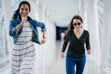 İki farklı arkadaş, iyi aydınlatılmış beyaz fütüristik bir üstgeçit köprüsünden kameraya doğru koşuyorlar. Biri Müslüman bir Orta Doğulu kadın, diğeri de Çinli..