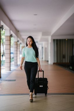 Genç bir Asyalı kadın bavulunu çekiyor. O çekici, zarif ve şık giyinmiş