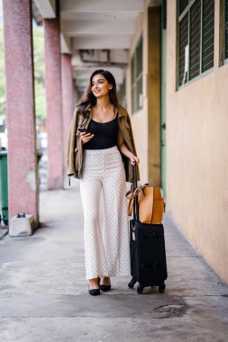 Genç ve çekici Asyalı Hint kadın arabayla aracılığıyla onun yolculuğu app onun akıllı yağıyor kitaplar. O bir geçit kendi bavullarla duruyor ve şık iş giysisi ve tonları giymiş