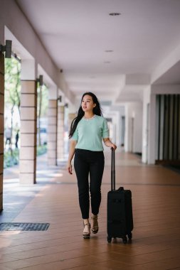 Genç bir Asyalı kadın bavulunu çekiyor. O çekici, zarif ve şık giyinmiş