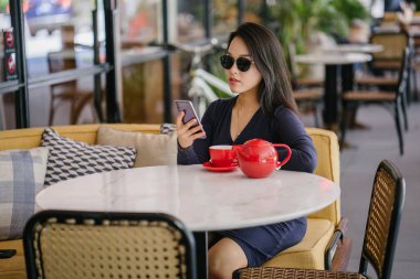 Bir açık havada açık havada oturan ve kırmızı bir çay seti çay sıcak bir fincan zevk genç, çekici, zarif ve güzel Asyalı kadın Portresi. 