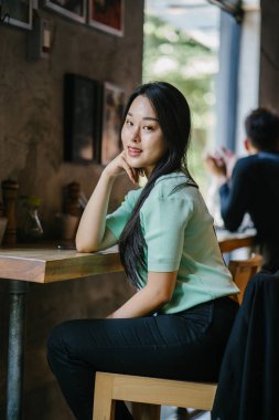 Genç ve çekici Çinli Asyalı bir kadının portresi uzanarak ve bir hafta sonu gün boyunca bir kafede rahatlatıcı. Nane yeşili bir kazak giyiyor.