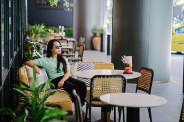 Genç ve çekici Çinli Asyalı bir kadının portresi uzanarak ve bir hafta sonu gün boyunca bir kafede rahatlatıcı. Nane yeşili bir kazak giyiyor.