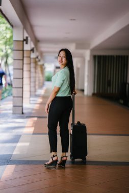 Genç bir Asyalı kadın bavulunu çekiyor. O çekici, zarif ve şık giyinmiş